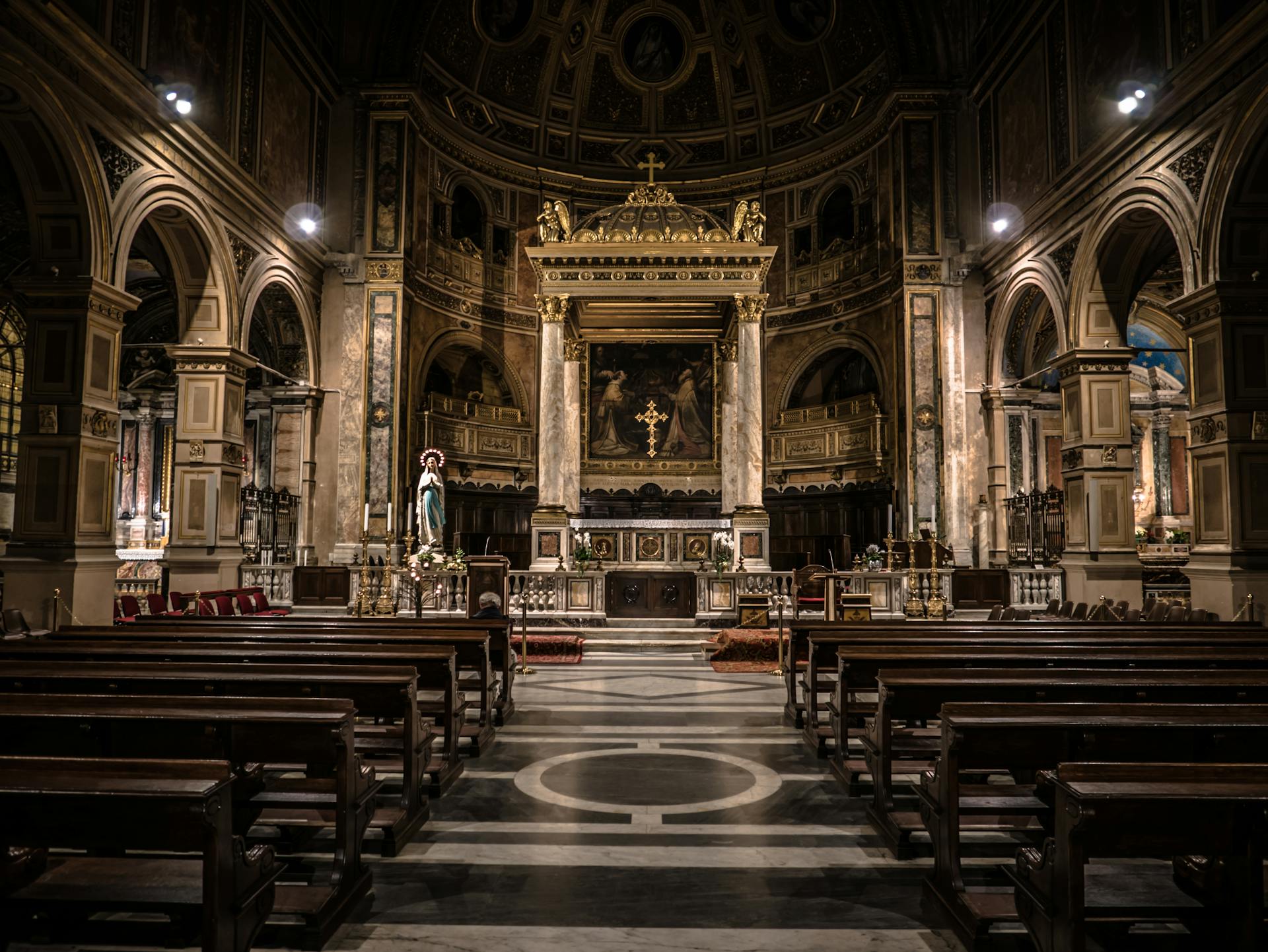 Interior of a gothic style catholic church. Statues, stained glass, old wooden pews, and roman architecture can be seen throughout,