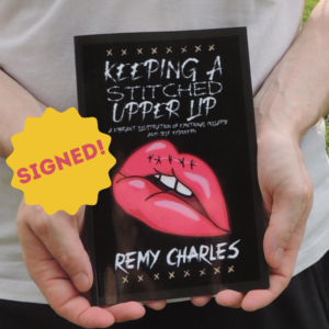 A pair of hands holding a paperback copy of Keeping A Stitched Upper Lip written by Remy Charles. A small starburst with the word "signed" written across it.