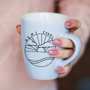 A mug featuring a black and white image of the sunrise or sunset over the horizon of a beach with lapping waves and clouds.